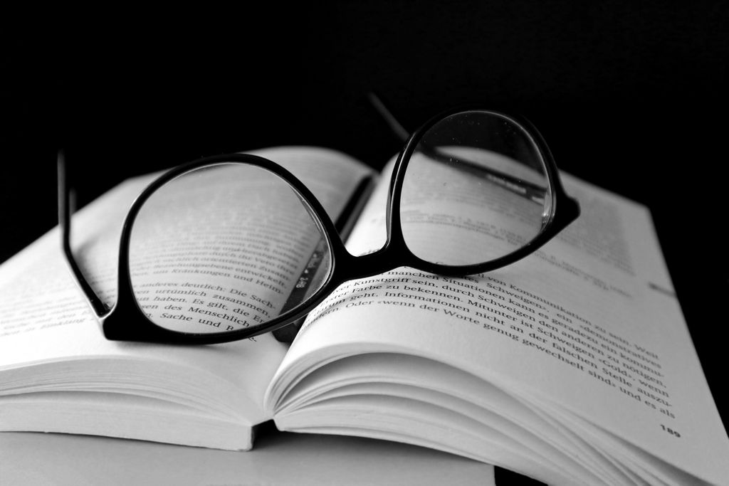 Open book with glasses on top, captured in dramatic black and white.